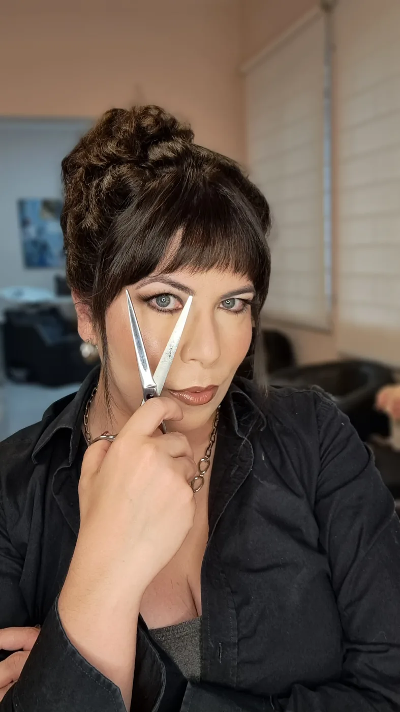 Marcela De Simone segurando uma tesoura aberta em frente ao rosto, no estúdio